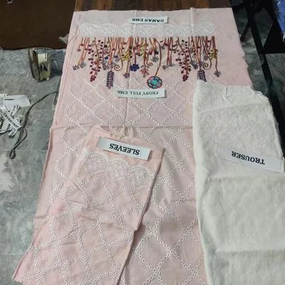 Two pieces of UrbanBaazar women's unstitched embroidered suit displayed on a hanger, showcasing intricate designs and fabric.